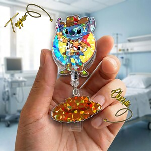 May include: A clear badge reel with a cartoon character design. The design features a blue alien character dressed as a cowboy, with a matching hat. A separate charm in the shape of a cowboy hat is attached to the reel.