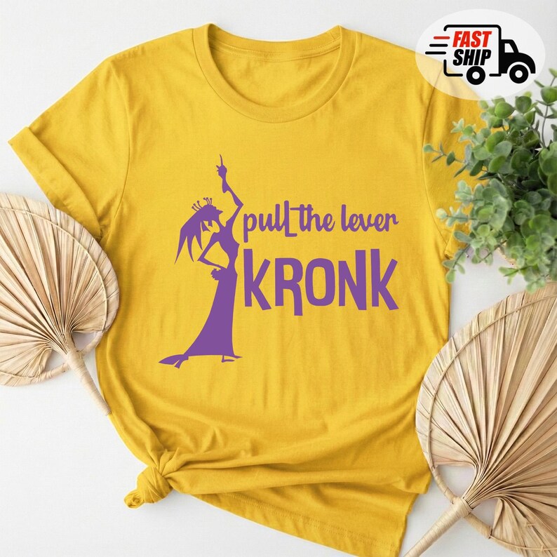 May include: Mustard yellow t-shirt with a purple graphic of a character and the text "pull the lever KRONK". The shirt is made of a soft material and has a crew neck.