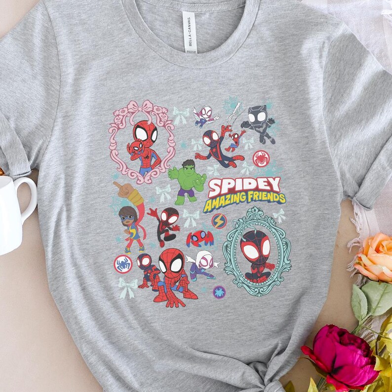 May include: A heather gray t-shirt featuring a colorful graphic of Spider-Man and other characters from the Spidey and His Amazing Friends series. The design includes the text "Spidey Amazing Friends" in yellow and green.