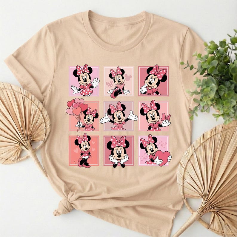 May include: A beige t-shirt with a grid of nine Minnie Mouse illustrations. Each Minnie Mouse is depicted in a pink dress and bow. The background squares alternate between pink and light pink.