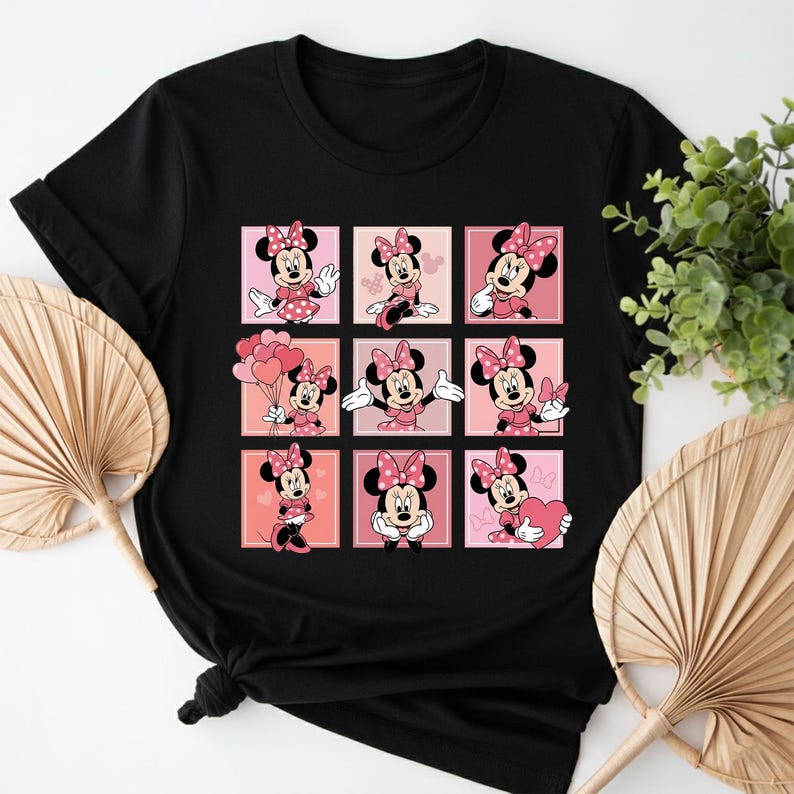 May include: Black t-shirt with a grid of nine Minnie Mouse illustrations in pink and red squares. Each square shows Minnie in different poses, wearing a pink bow and dress. The shirt is made of a soft material.