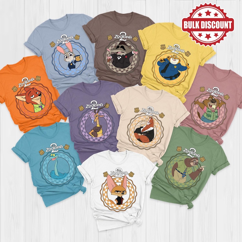K&ouml;nnte beinhalten: Eine Sammlung von T-Shirts zum Thema Zootopia in verschiedenen Farben, jedes mit einem anderen Charakter in einem kreisf&ouml;rmigen Design. Die Shirts sind kurz&auml;rmlig und aus einem weichen Material. Das Bild enth&auml;lt ein "Bulk Discount"-Siegel.