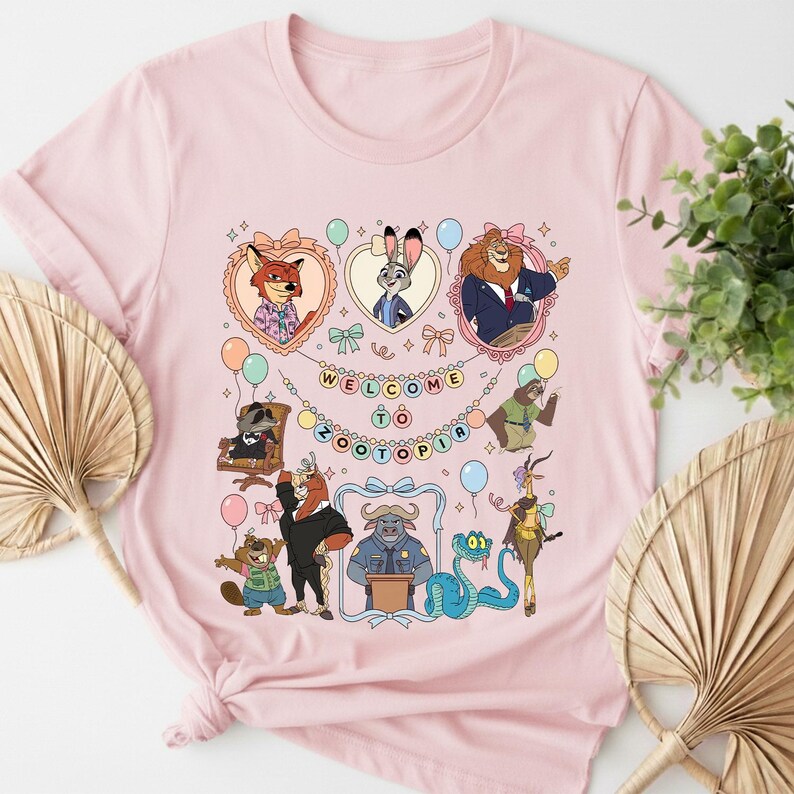 Puede incluir: Camiseta rosa claro con un dise&ntilde;o colorido de personajes de Zootopia. El dise&ntilde;o incluye animales de dibujos animados en marcos con forma de coraz&oacute;n, globos y la frase "WELCOME TO ZOOTOPIA". Un dise&ntilde;o divertido para los fans de la pel&iacute;cula animada.