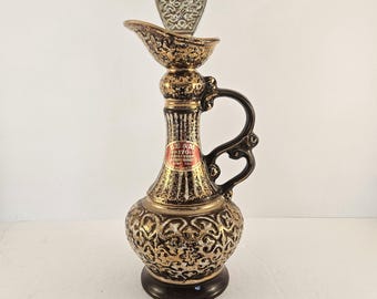 Op de afbeelding: Een vintage karaf met een decoratief goud- en bruin ontwerp. De karaf heeft een handvat en een tuit en is bekroond met een zilverkleurige stop. De basis is donkerbruin. De karaf heeft een label met de tekst "BEAM 1795".