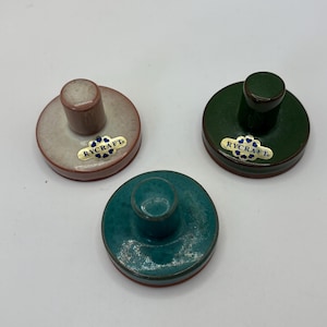 May include: Three circular ceramic stamps with handles, each featuring a gold-colored label with the text RYCRAFT. One stamp is light beige, one is dark green, and one is a teal blue color. Each stamp has a smooth, glazed finish on top.