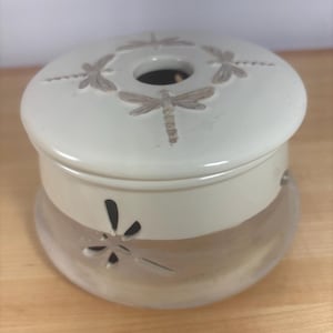 May include: A cream-colored essential oil diffuser with a frosted glass base and a matching lid. The lid features embossed dragonfly designs around a central opening. The base has dragonfly cutouts, and the diffuser sits on a wooden surface.