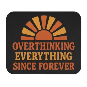 May include: Black mousepad with a retro design featuring a rising sun in shades of orange and yellow. The text "OVERTHINKING EVERYTHING SINCE FOREVER" is printed in orange and yellow.