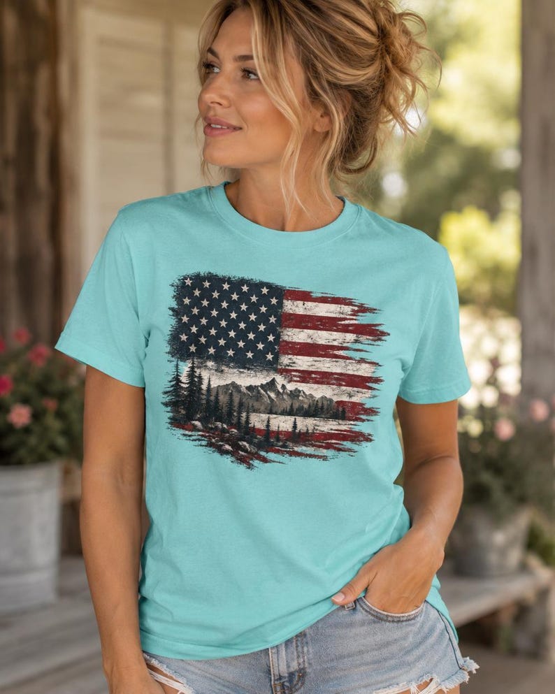 Woman wearing patriotic mountain flag graphic Comfort Colors t shirt with distressed denim shorts on farmhouse porch