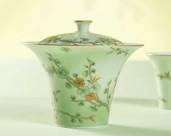 Puede incluir: Una taza de té de porcelana verde pálido con tapa a juego. La taza y la tapa están decoradas con un diseño floral en tonos verdes y dorados. La taza tiene forma acampanada y borde dorado.