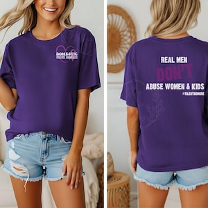 Könnte beinhalten: Ein violettes Kurzarm-T-Shirt mit einer kleinen weißen und violetten Schleife zur Sensibilisierung für häusliche Gewalt auf der Brust und dem Text "REAL MEN DON'T ABUSE WOMEN & KIDS #SILENTNOMORE" in Weiß und Violett auf dem Rücken.