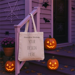 May include: A cream-colored tote bag with the text "Homeglow Mockups YOUR DESIGN HERE" hangs on a purple porch railing. Two carved orange pumpkins with lit faces sit on the steps, with a spider web and bats for Halloween.