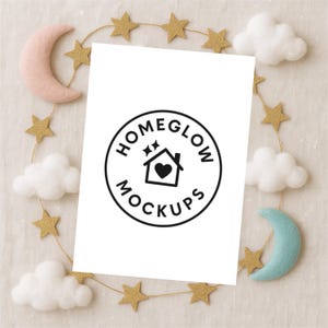 Puede incluir: Un papel blanco con un logotipo circular negro que dice "HOMEGLOW MOCKUPS" rodea una casa con un corazón en su interior. El papel está rodeado por una guirnalda de estrellas doradas, nubes blancas y lunas de fieltro en rosa y azul.