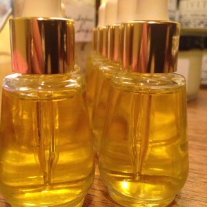 May include: Five small glass bottles with gold lids and droppers filled with a clear yellow liquid. The bottles are arranged in a row on a wooden surface.