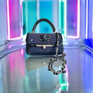 May include: A small, dark blue handbag with a beaded handle and a decorative beaded chain. The bag is embellished with sequins and a floral design. The background features neon lights in shades of pink, blue, and purple.