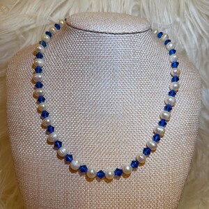May include: A delicate necklace featuring white pearls and vibrant blue crystal beads. The beads are interspersed along the necklace's length, creating a striking contrast. The necklace is displayed on a neutral-toned mannequin.