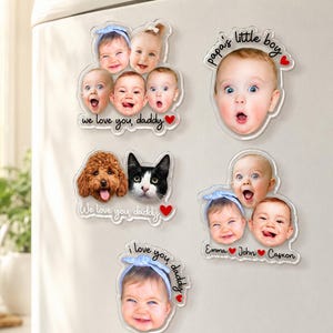 May include: A collection of clear acrylic magnets featuring photos of babies, a dog, and a cat. Some magnets have text that reads "we love you, daddy," "papa's little boy," and "i love you, daddy." The magnets are attached to a white surface.