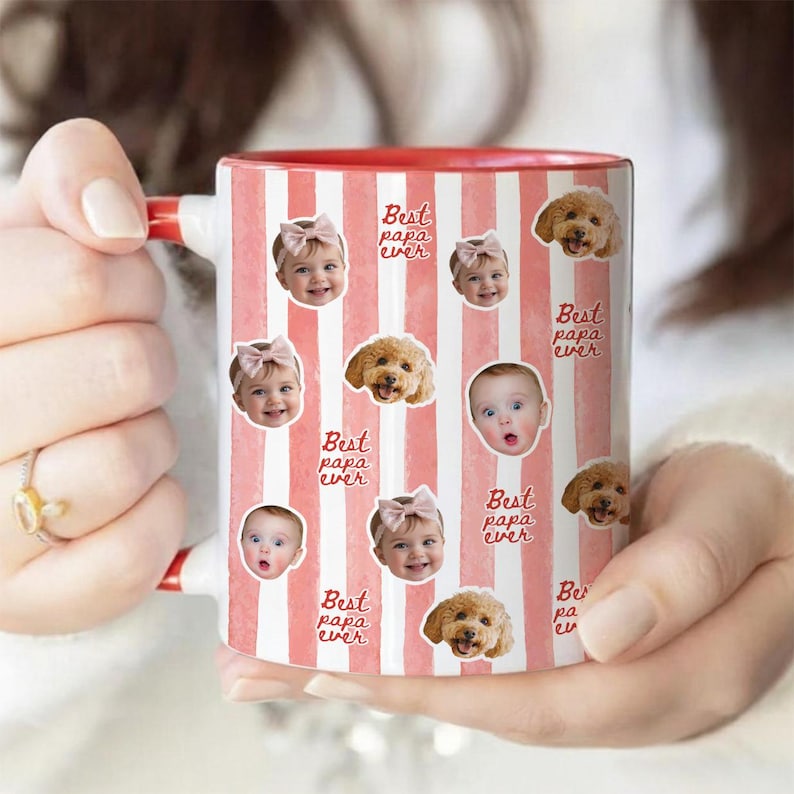 May include: A white ceramic mug with vertical pink stripes featuring a repeating pattern of baby faces wearing pink bows and brown dog faces. The text "Best papa ever" is printed in a cursive red font throughout the design of the mug.