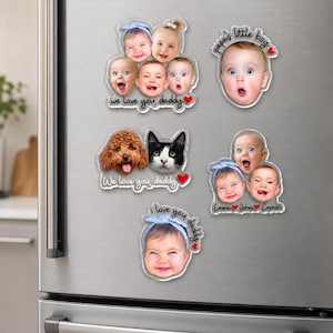 May include: Five custom acrylic photo magnets featuring portraits of babies, a dog, and a cat. Text includes "we love you, daddy", "papa's little boy", "i love you, daddy", and names "Emma", "John", and "Caxon" with red heart accents on a silver surface.