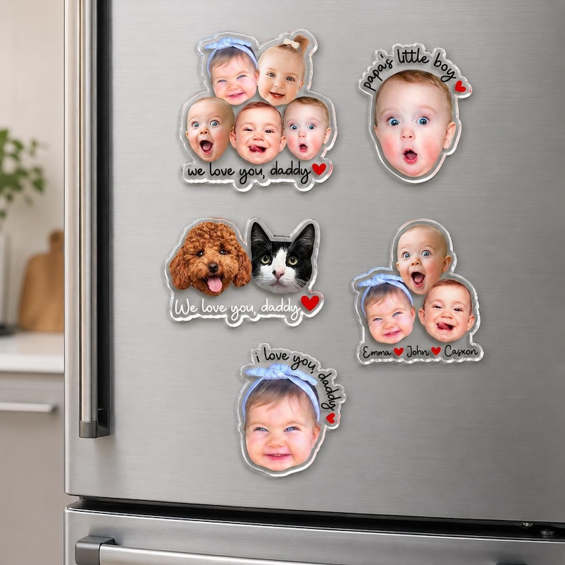 May include: Five custom acrylic photo magnets featuring portraits of babies, a dog, and a cat. Text includes "we love you, daddy", "papa's little boy", "i love you, daddy", and names "Emma", "John", and "Caxon" with red heart accents on a silver surface.