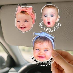 Puede incluir: Tres clips de acr&iacute;lico personalizados para visera de coche con retratos fotogr&aacute;ficos de beb&eacute;s. Un beb&eacute; lleva un lazo color melocot&oacute;n, otro tiene una expresi&oacute;n de sorpresa con el texto drive safe, daddy, y otro lleva una diadema azul con el texto drive safe, papa.
