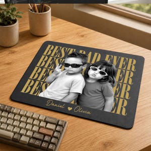 May include: A rectangular black mousepad featuring a repeating gold text pattern that reads BEST DAD EVER. The center displays a black and white photograph of two children wearing sunglasses. The names Daniel and Olivia are printed in gold script.