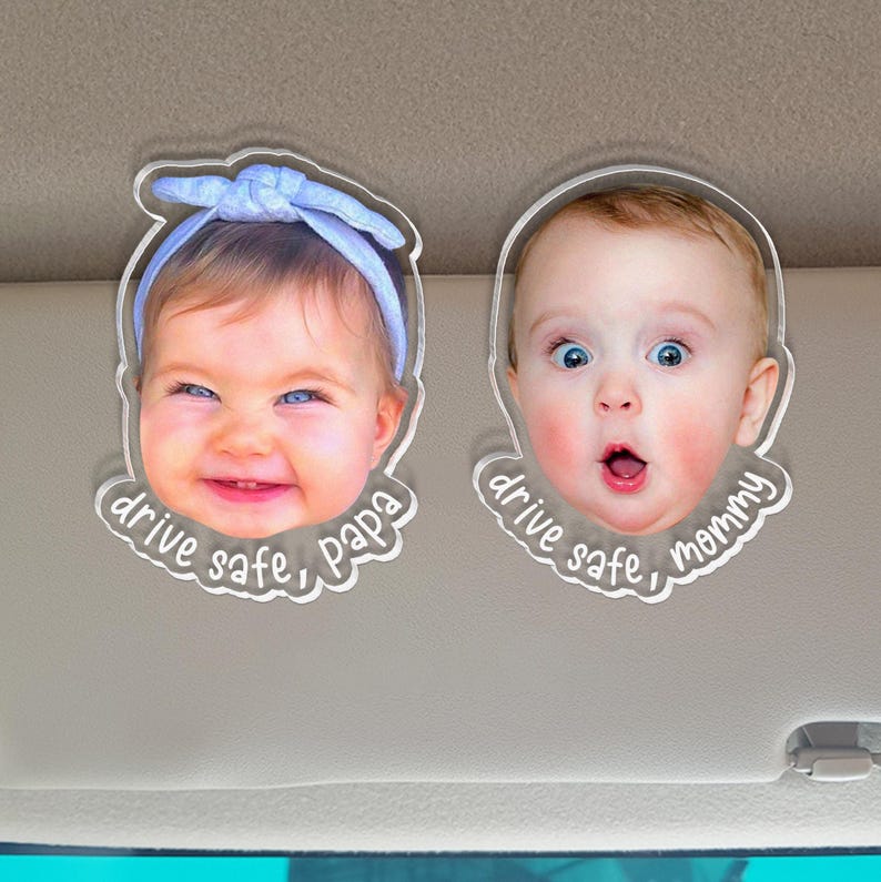 Puede incluir: Dos clips de acr&iacute;lico transparente para visera con caras de beb&eacute; impresas. El clip izquierdo muestra a un beb&eacute; con una diadema azul claro y el texto drive safe, papa. El derecho muestra a un beb&eacute; con la boca abierta y el texto drive safe, mommy.