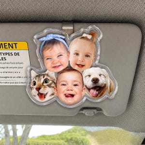 Puede incluir: Un clip de acr&iacute;lico transparente para visera de coche con cinco recortes fotogr&aacute;ficos circulares de tres beb&eacute;s y dos mascotas, incluyendo un gato atigrado y un perro de color claro. Los beb&eacute;s muestran expresiones faciales, uno lleva una diadema azul y otro un peque&ntilde;o lazo.