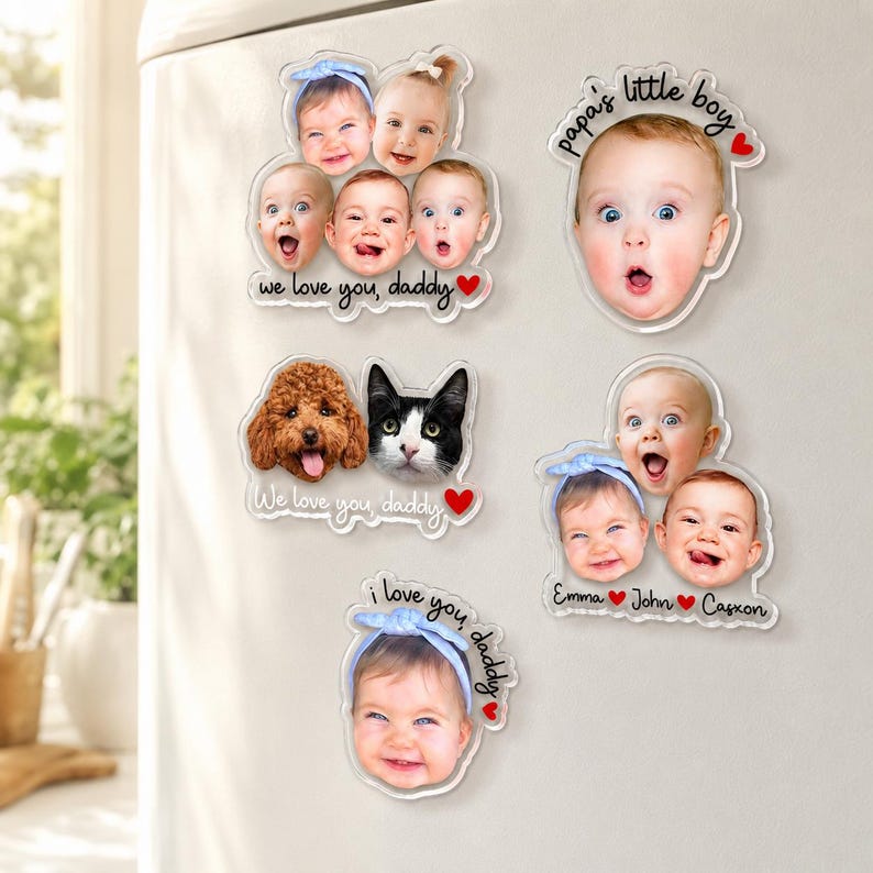 May include: A collection of clear acrylic magnets featuring photos of babies, a dog, and a cat. Some magnets have text that reads "we love you, daddy," "papa's little boy," and "i love you, daddy." The magnets are attached to a white surface.