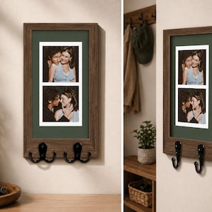 May include: A rectangular wall-mounted picture frame with a dark wood finish and a dark green mat. The frame holds two vertical photographs of a couple and features two black metal double hooks attached to the bottom edge for hanging items.