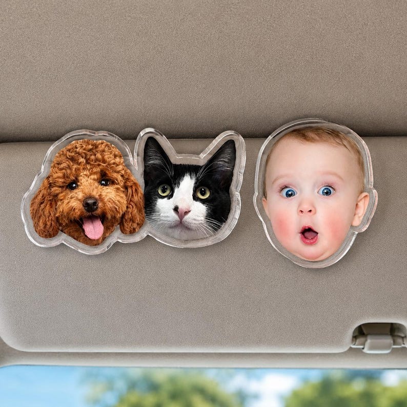 Puede incluir: Dos clips de acr&iacute;lico personalizados para visera de coche con retratos fotogr&aacute;ficos. Un clip muestra un perro marr&oacute;n de pelo rizado y un gato blanco y negro juntos. El segundo clip presenta el retrato de un beb&eacute; con expresi&oacute;n de sorpresa.