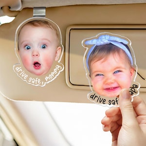 Puede incluir: Dos clips de acr&iacute;lico transparente para visera de coche con recortes de fotos personalizados de beb&eacute;s. Uno muestra a un beb&eacute; con expresi&oacute;n de sorpresa y el texto drive safe, mommy. El otro muestra a un beb&eacute; sonriente con una diadema azul y el texto drive safe, papa.