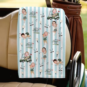 May include: A light blue and white striped golf towel featuring a repeating pattern of cartoon figures with photographic faces, golf carts, golf clubs, golf balls, and the text "Best Dad By Par" printed in a dark blue script font.