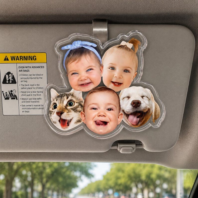 Puede incluir: Un accesorio de acr&iacute;lico transparente para el parasol del coche que presenta un collage de cinco retratos circulares, incluyendo tres beb&eacute;s y dos animales. Los beb&eacute;s tienen diversas expresiones y accesorios como una diadema azul y un lazo blanco.