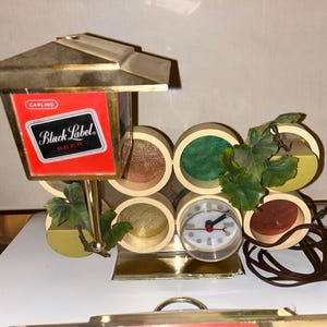 May include: Vintage Black Label Beer advertising display with a clock. The display features a red and black sign with the Black Label Beer logo, a clock, and decorative wooden elements. The display has a gold-colored metal frame.