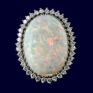 May include: An oval opal gemstone ring, surrounded by a halo of small, round, clear diamonds. The opal displays a milky white base with colourful flashes. The ring is set against a dark blue backdrop.