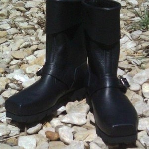 May include: A pair of black leather boots with buckles and a thick sole. The boots have a fold-over top and are made of a durable material.