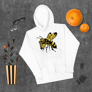 Könnte beinhalten: Ein weißer Kapuzenpullover mit einem Grafikdruck auf der Brust, der eine gelb-schwarze Biene mit Gasmaske zeigt. Der Hoodie verfügt über eine Kängurutasche auf der Vorderseite, lange Ärmel und eine Kapuze mit Kordelzug.