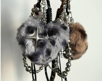 May include: A collection of keychains featuring fluffy, heart-shaped charms in gray and brown, adorned with silver-toned embellishments like crosses, stars, and beaded chains. The keychains have black cords and silver key rings.