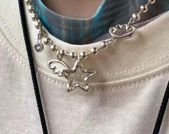 May include: Silver-toned necklace with a ball chain design. The necklace features a star pendant with wings and a small purple gemstone charm. The necklace is worn over a white t-shirt.
