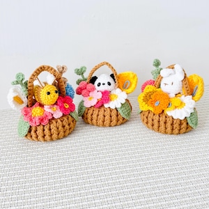 May include: Three handmade crochet baskets, each filled with colorful flowers and a small animal figure. The baskets are brown with handles, and the flowers are pink, yellow, and white. One basket has a bee, another a panda, and the last a bunny.