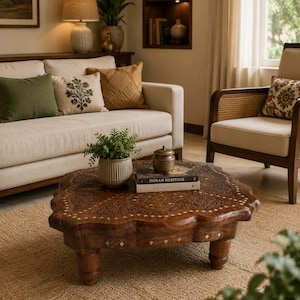 May include: A low, square wooden coffee table with scalloped edges, intricate floral carvings, and inlaid brass diamond accents. The table features four sturdy, rounded legs and supports a small potted plant and two stacked books.