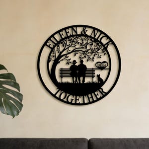 Könnte beinhalten: Schwarze Metall-Wandkunst mit einem Paar auf einer Bank unter einem Baum, mit einer Katze und dem Wort "TOGETHER". Die Namen "EILEEN & NICK" und das Jahr "1984" sind ebenfalls enthalten.