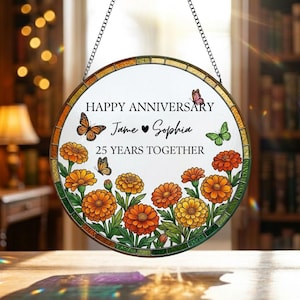 May include: Round, stained-glass anniversary plaque with a chain for hanging. The plaque features the text "HAPPY ANNIVERSARY" and "25 YEARS TOGETHER", with names "Jane ♥ Sophia". Orange flowers and butterflies decorate the design.