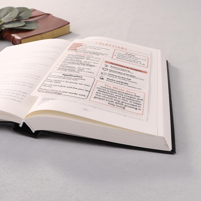 May include: An open book with black covers, displaying pages with text and highlighted sections. The text includes the word "Colossians" and other religious terms. A brown leather-bound notebook is visible in the background.