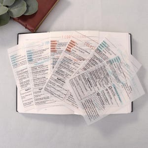 May include: Open book with several transparent sticky notes with text. The notes have titles like "1 Corinthians" and "Colossians". The text includes words like "Application" and "Epistle". A brown leather-bound book is visible.