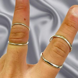 Può includere: Quattro anelli sottili in metallo color argento lucido indossati su due dita. Ogni dito presenta due fasce circolari lisce posizionate ad altezze diverse, caratterizzate da una finitura metallica semplice e riflettente senza pietre o incisioni.