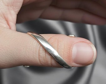 May include: A silver-colored thumb ring with a curved design. The ring wraps around the thumb, with small connecting pieces on the top and bottom of the thumb. The ring is shown on a person's thumb.