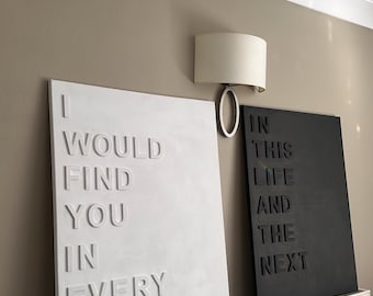 May include: Two rectangular wall art pieces with embossed text. One is white and reads "I WOULD FIND YOU IN EVERY LIFETIME." The other is black and reads "IN THIS LIFE AND THE NEXT."