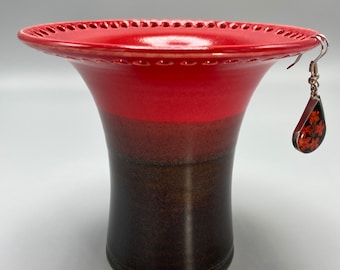 May include: A red and black ceramic vase with a decorative rim and a small earring hanging from the rim.