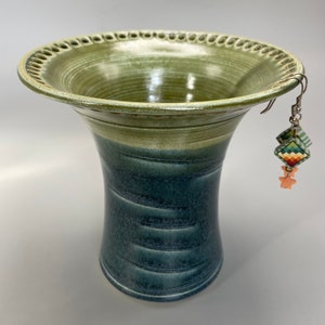 May include: A green and blue ceramic vase with a decorative rim and a pair of earrings hanging from the rim.